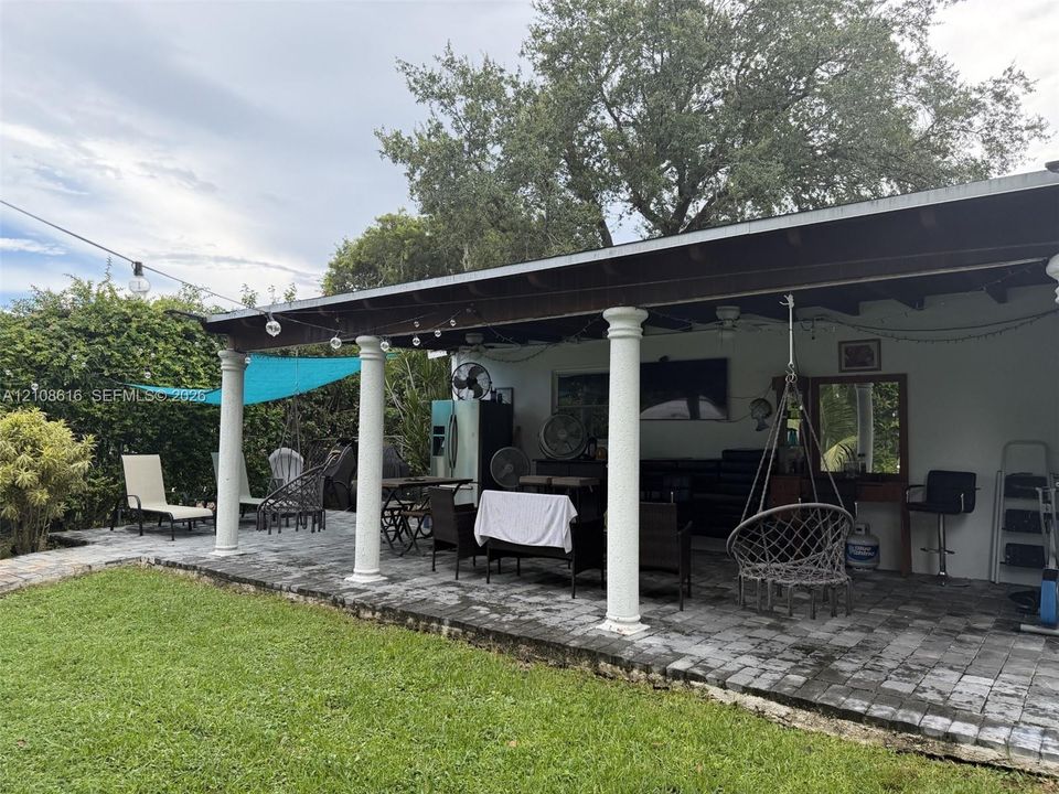 Covered patio featuring stone paver flooring, structural columns, and an expansive lawn