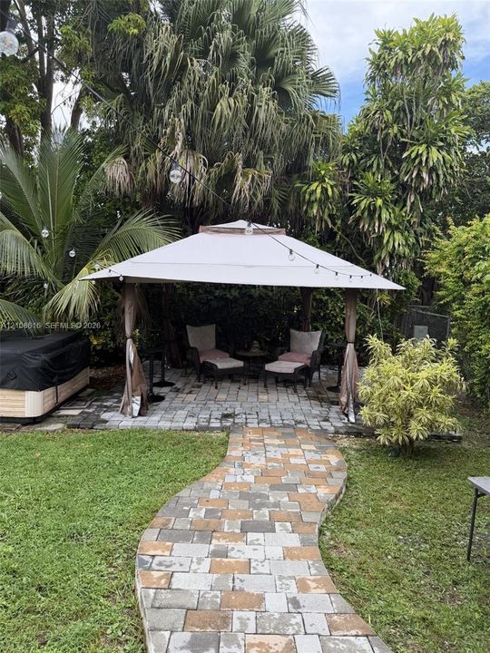 Backyard space featuring a paver stone walkway, a structured gazebo, a hot tub, and mature landscaping