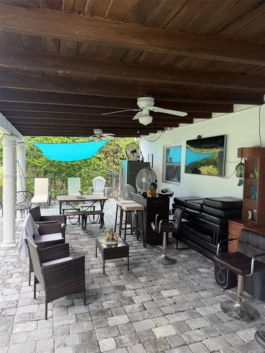 Covered patio featuring an exposed wood-beam ceiling, stone paver flooring, classic columns, and dual ceiling fans