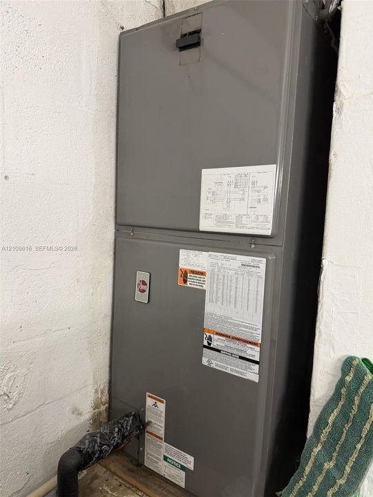Gray Rheem heating and cooling air handler unit mounted against white painted masonry walls