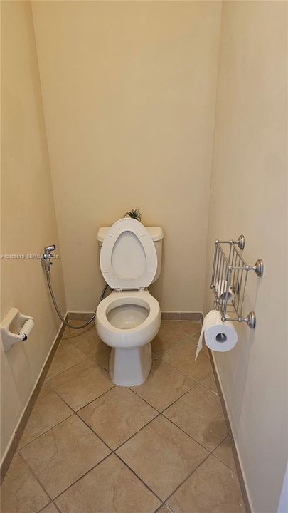 Porcelain toilet with bidet attachment, ceramic tile flooring, and wall-mounted metal toilet paper holder and shelving unit