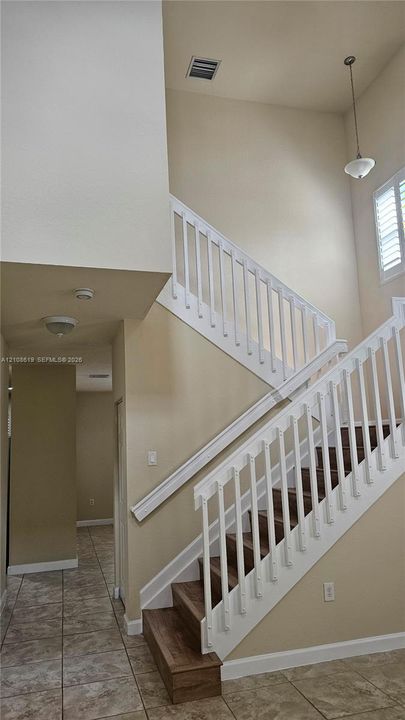 Staircase featuring wood-finish treads, white balusters, high ceilings, tile flooring, and a pendant light fixture