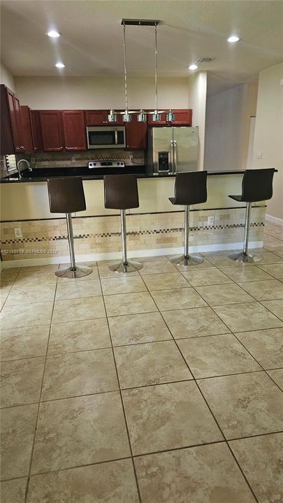 Kitchen featuring a peninsula island, stainless steel appliances, tile flooring, stone-tiled backsplash, and overhead pendant lighting