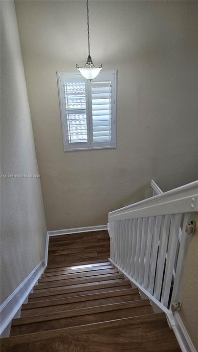Staircase featuring wood-finish treads, a white balustrade, a window with interior shutters, and a pendant light fixture