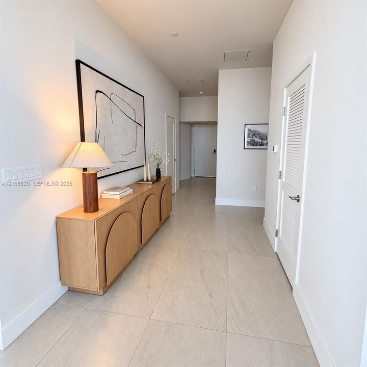 Entry hallway featuring large-format neutral tile flooring, high ceilings, and louvered-style interior doors