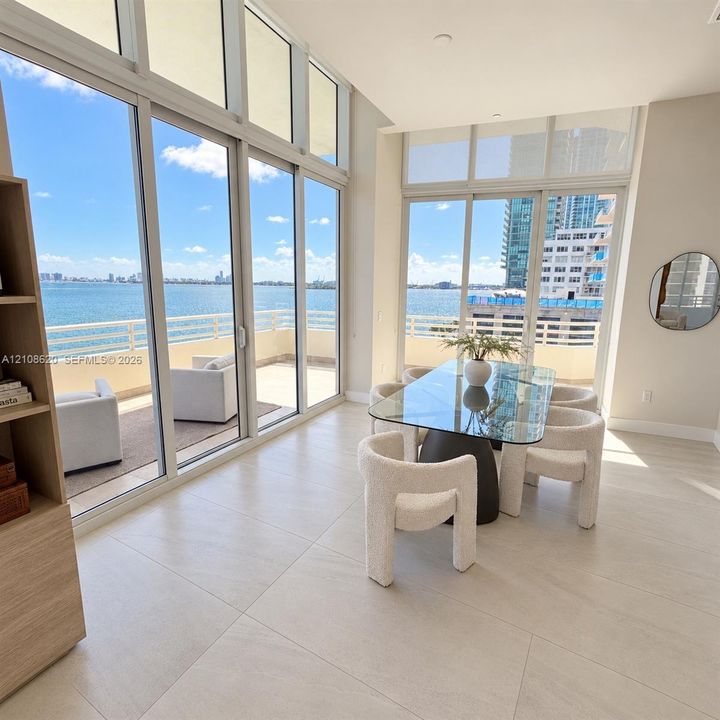 Floor-to-ceiling windows featuring expansive water scenery, large-format tile flooring, and a glass-enclosed balcony with railing