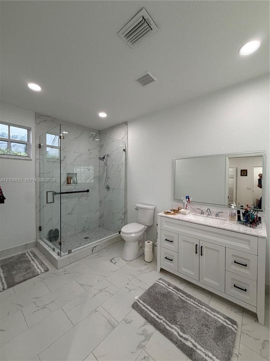 Bathroom featuring a glass-enclosed walk-in shower with tile surround, white vanity with stone countertop, recessed lighting, and large-format tile flooring