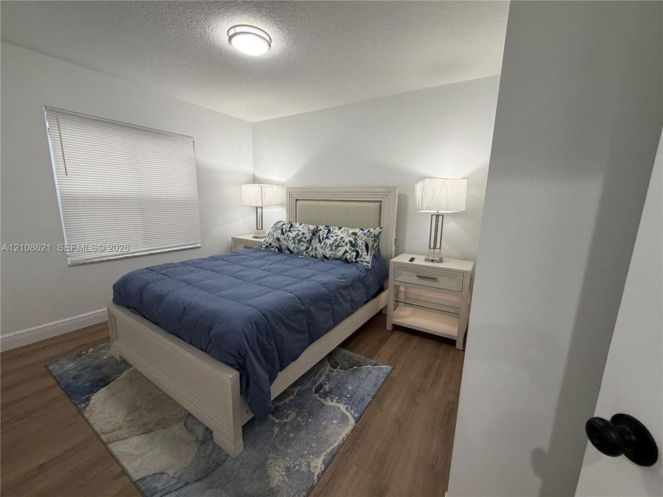 Neutral wall tones, wood-finish flooring, and flush-mount ceiling lighting, complemented by a window with horizontal blinds