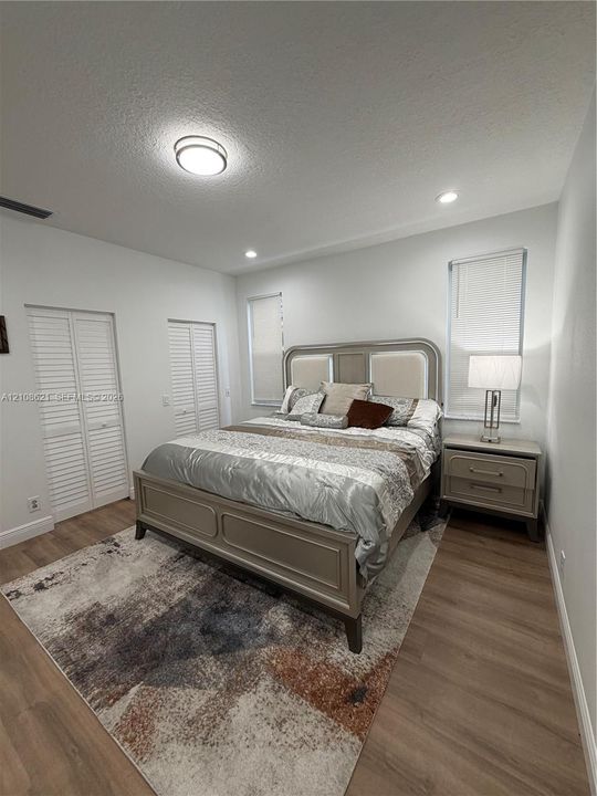 Room featuring wood-finish flooring, dual white louvered-style closet doors, recessed lighting, and windows equipped with horizontal blinds
