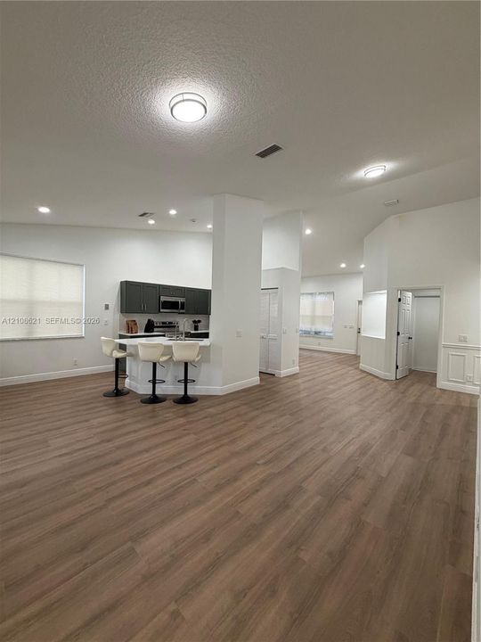 Open-concept interior featuring wood-finish flooring, dark cabinetry, recessed lighting, and a breakfast bar with stone-surface countertop