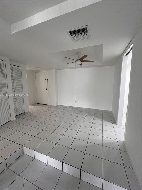 Interior space featuring large-format ceramic tile flooring, a tray ceiling, a ceiling fan, and dual louvered closet doors