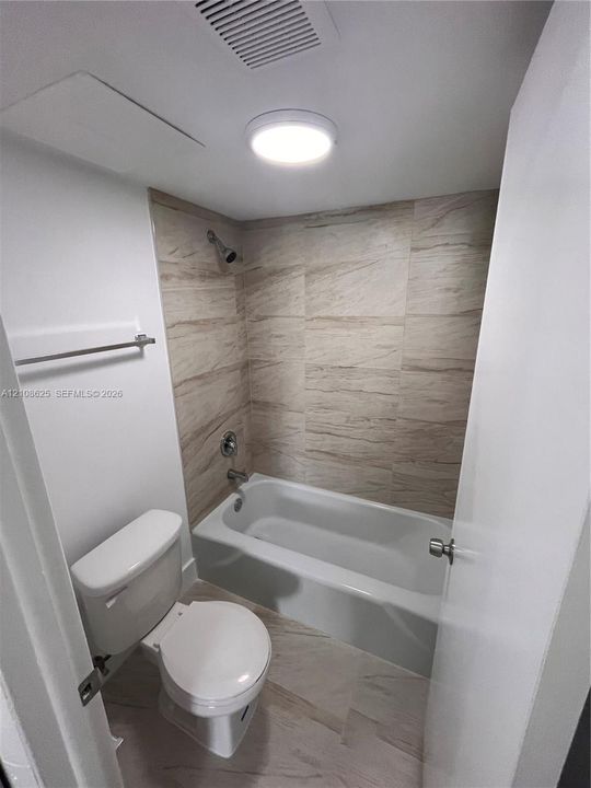 Bathroom featuring a tub with a neutral-toned tile surround, flush-mount lighting, and wall-mounted towel bar