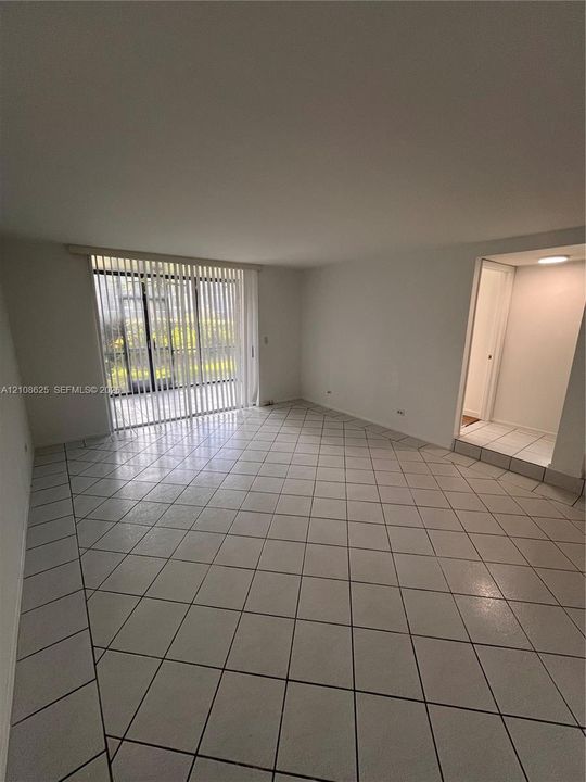 Open interior featuring large-format diagonal tile flooring, sliding glass patio doors with vertical blinds, and recessed ceiling lighting