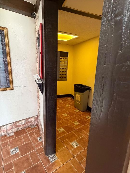 Textured wall surfaces, dark wood-finish structural trim, square ceramic tile flooring with decorative inlay accents, and built-in metal mailboxes