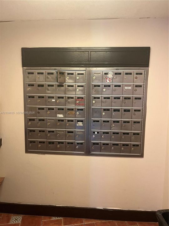 Wall-mounted cluster mailbox unit featuring dual stainless steel banks with individual key-locked compartments and dark-finish header trim