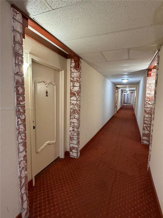 Hallway featuring decorative brick-clad columns, wood-beam accents, and recessed lighting