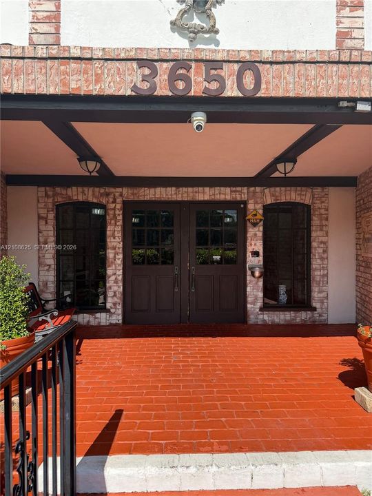 Covered entryway featuring a painted brick porch, double wood-panel doors with glass panes, arched windows, and an exposed beam ceiling