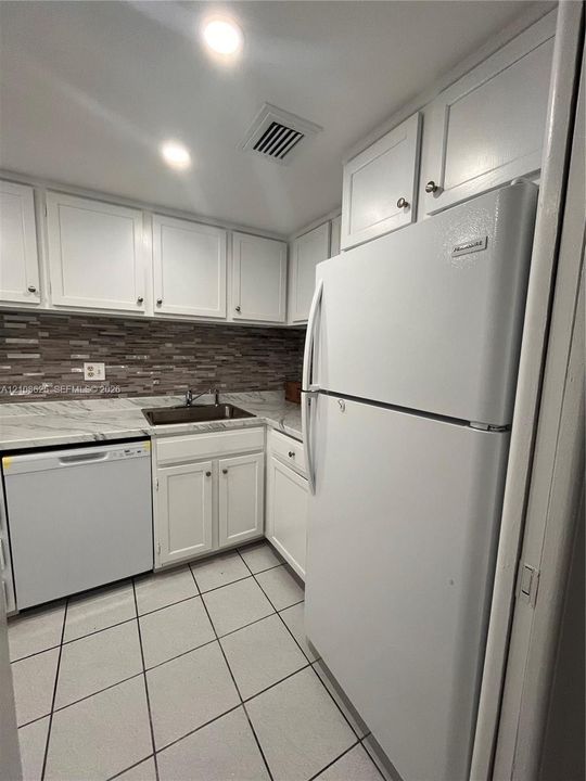 Kitchen featuring white cabinetry, stone-patterned countertops, a decorative mosaic tile backsplash, a stainless steel sink with a high-arch faucet, and square ceramic tile flooring