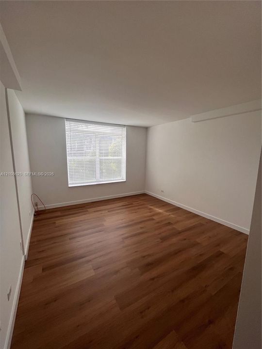 Interior room featuring wood-finish flooring, neutral walls, and a single window with installed horizontal blinds