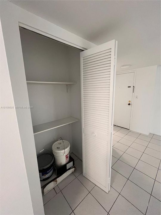 Storage closet featuring louvered bi-fold doors and interior shelving, set above white tiled flooring
