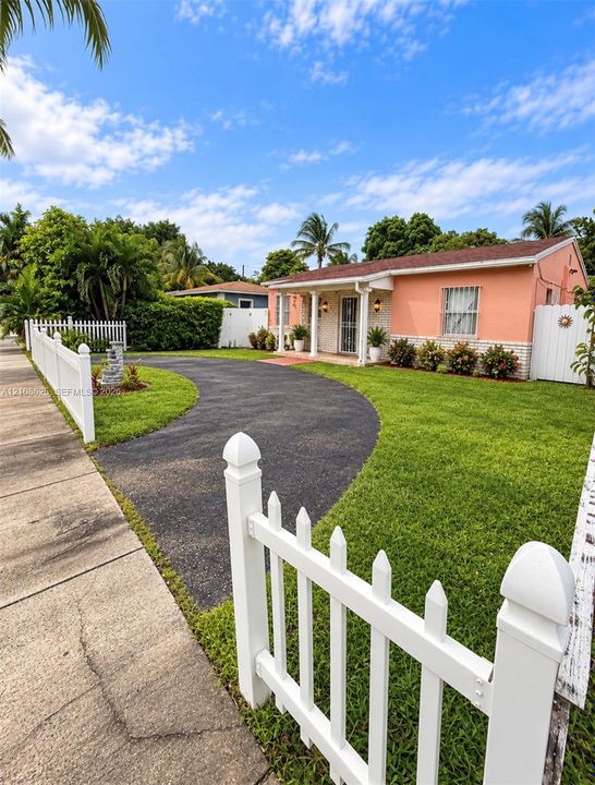 Single-story exterior featuring stucco and brick facade, a curved asphalt driveway, and perimeter white picket fencing