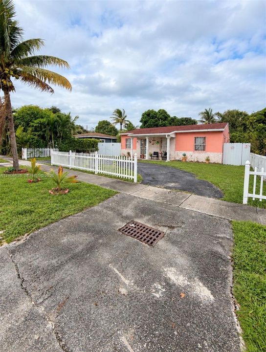 Single-story exterior featuring a vibrant stucco finish, stone-veneer foundation, covered front porch with columns, white picket fencing, and paved driveway