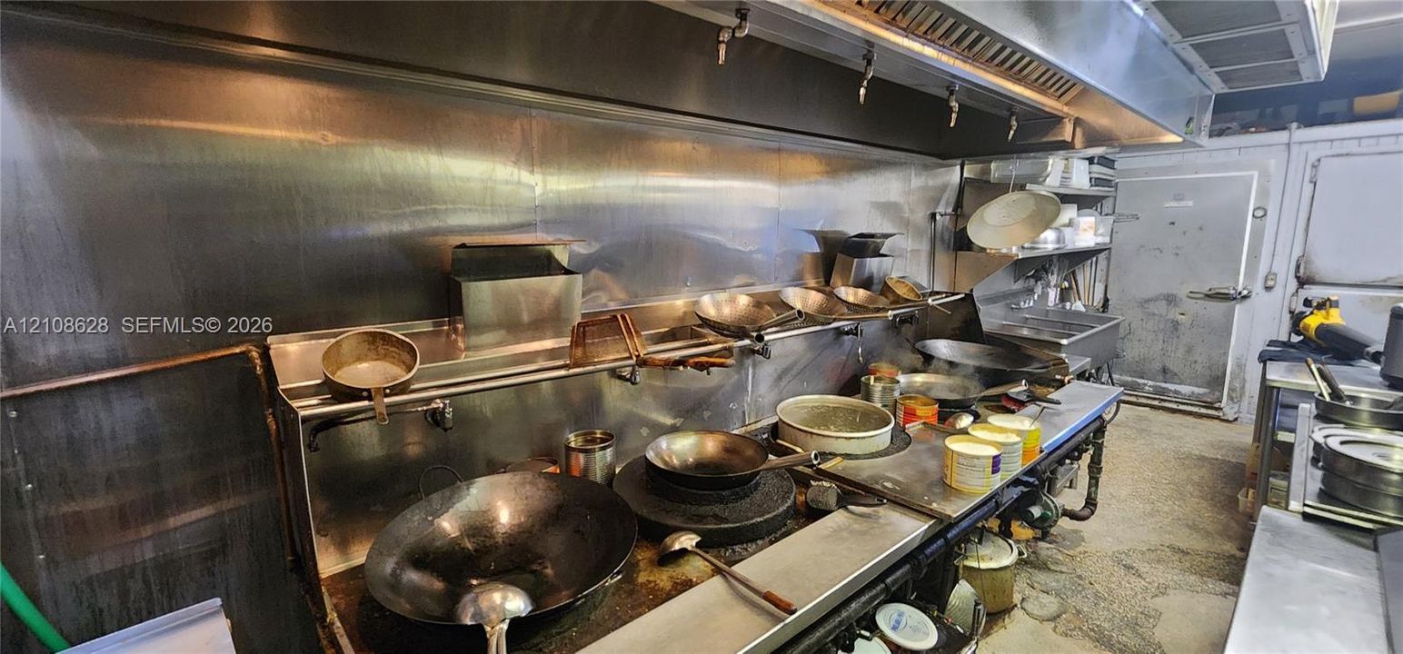 Commercial-grade stainless steel kitchen featuring a heavy-duty exhaust hood, metal backsplash, and industrial walk-in refrigeration unit