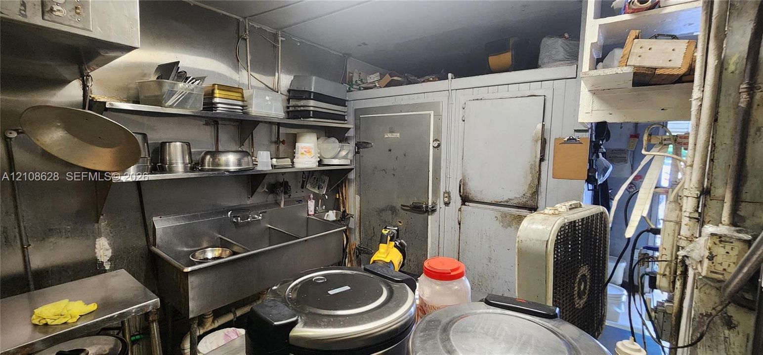 Commercial kitchen area featuring a stainless steel multi-compartment sink, stainless steel wall shelving, and an integrated walk-in cold storage unit