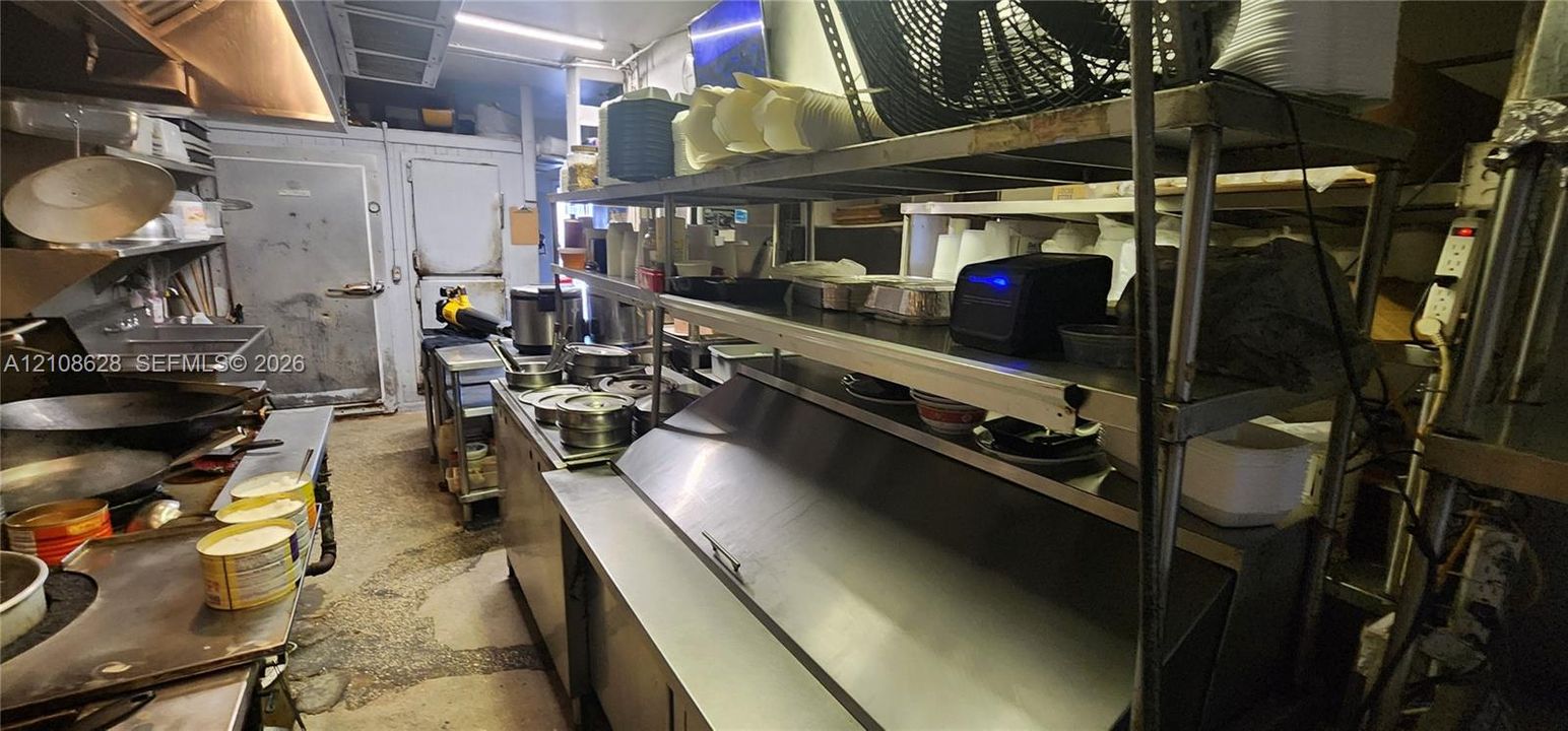 Commercial kitchen featuring stainless steel prep surfaces, multi-tiered metal shelving, integrated refrigeration unit, and metal basin sink
