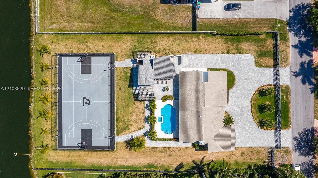 Waterfront property featuring a fenced sport court, swimming pool with attached spa, pergola, and extensive paved driveway