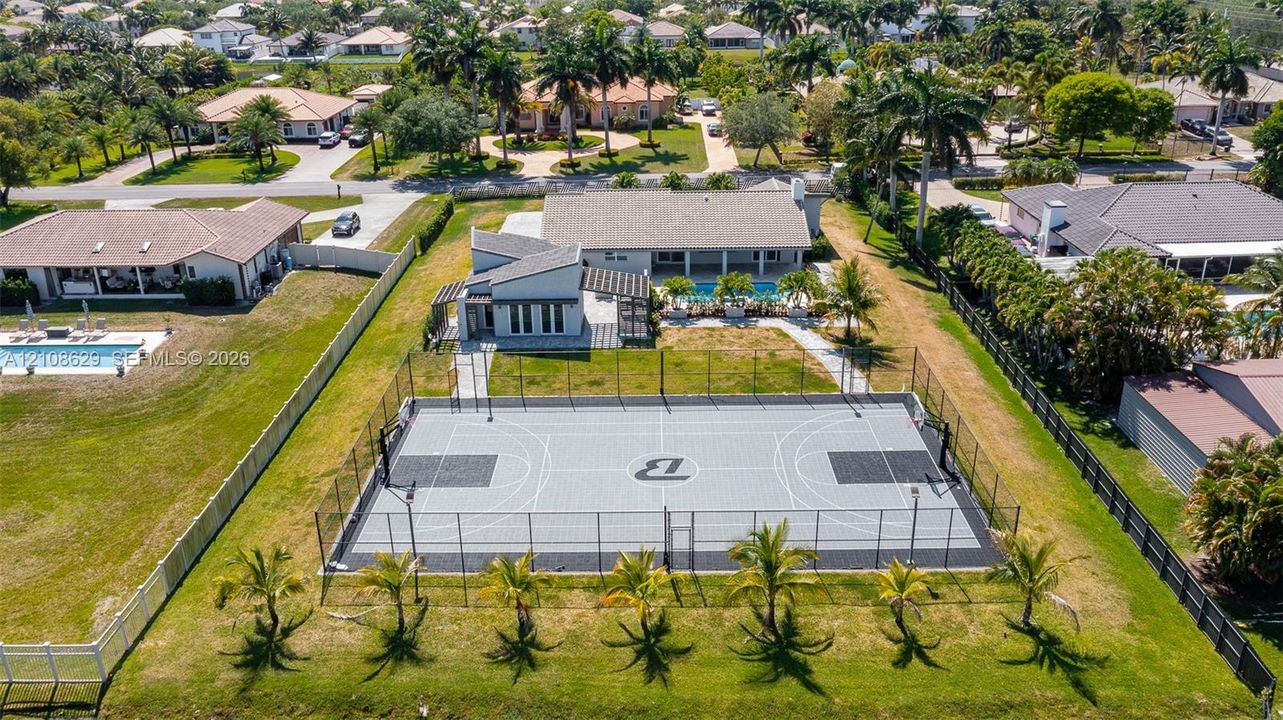 Private fenced basketball court with modular surfacing, expansive rear grounds, mature palm trees, and swimming pool