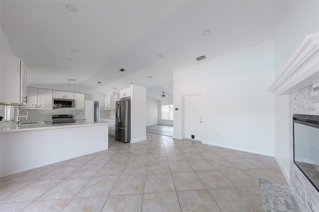 Kitchen featuring white shaker-style cabinetry, a stone tile backsplash, a peninsula with a quartz countertop, tile flooring, and a fireplace with a stone veneer surround