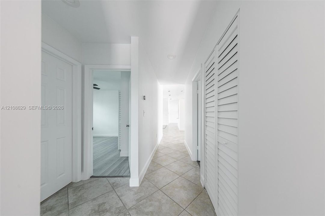Hallway featuring neutral large-format tile flooring, louvered bi-fold closet doors, and recessed ceiling lighting