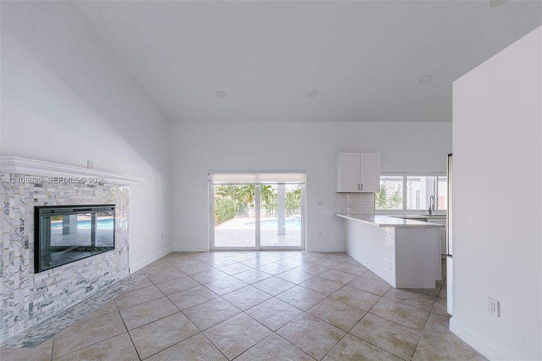 Open-concept space featuring tile flooring, stone-surround fireplace with a mantel, recessed lighting, and a breakfast bar with stone-finish countertops
