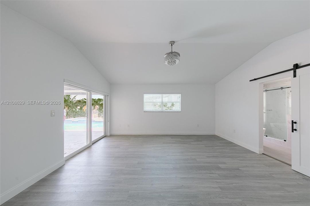 Vaulted ceilings with a centralized ceiling fan, wood-finish flooring, sliding glass doors, and a sliding barn-style door