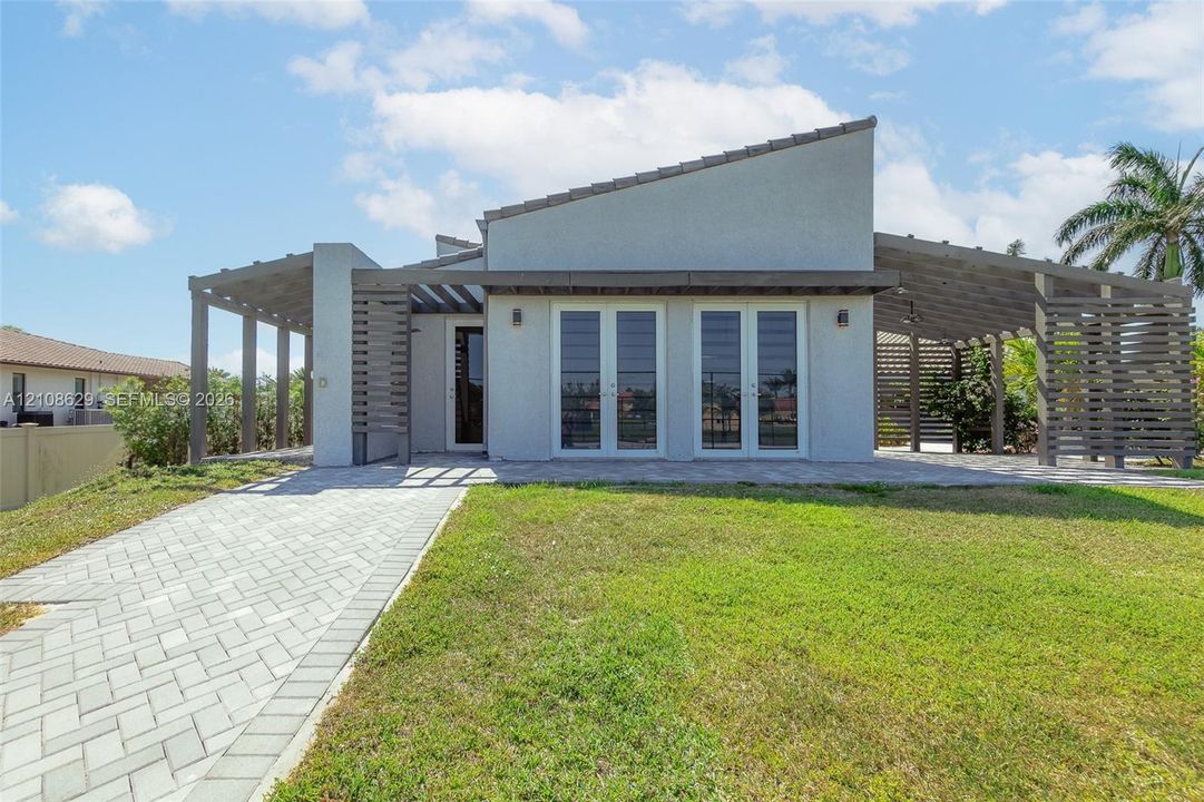 Modern exterior featuring a shed-style roofline, dual wood-finish pergolas, paver hardscaping, and double glass-paned doors