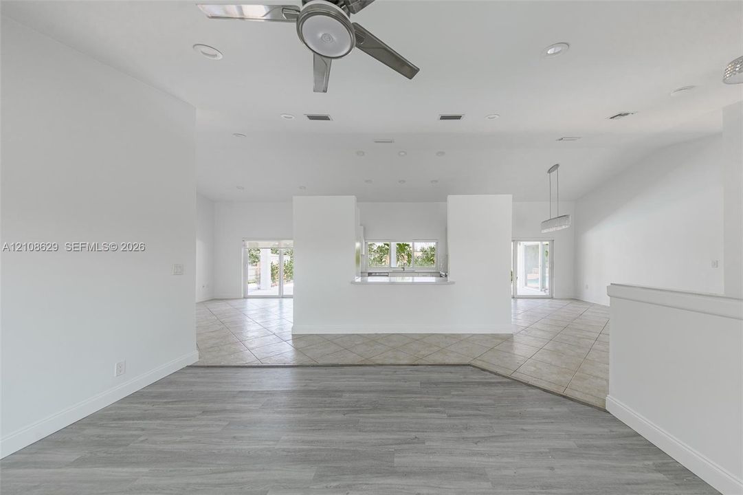 Open-concept interior featuring wood-finish flooring, ceramic tile flooring, a central partition wall with a pass-through counter, recessed lighting, and a ceiling fan