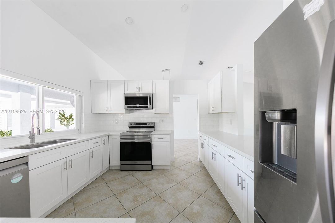 Kitchen featuring white cabinetry, solid-surface countertops, tile flooring, stainless steel appliances, and a double-basin sink