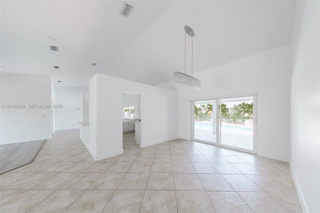Open-concept interior featuring vaulted ceilings, oversized tile flooring, a contemporary linear chandelier, and sliding glass doors