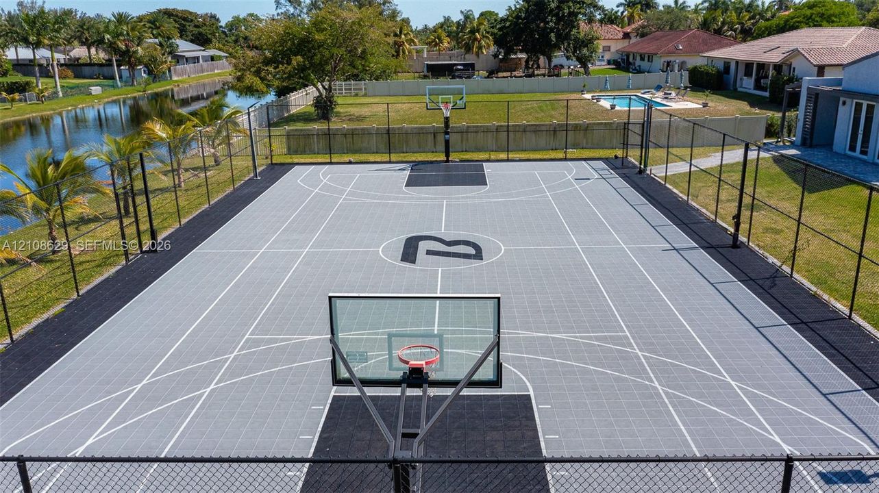 Private outdoor basketball court featuring interlocking modular surface tiles, perimeter chain-link fencing, and dual glass backboards with metal rims