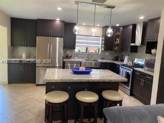 Kitchen featuring dark cabinetry, a central island with stone-finish countertops, a stainless steel apron-front sink, recessed lighting, and a triple-pendant fixture