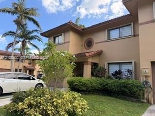 Stucco exterior featuring clay tile roofing, decorative circular window detailing, and manicured landscaping
