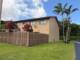 Two-story exterior featuring a stucco facade, a privacy-fenced enclosure, manicured lawn, and mature palm trees