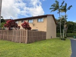 Stucco exterior featuring a wood-style privacy fence, manicured lawn, and established palm trees