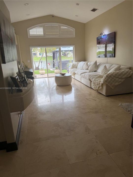 Vaulted ceiling featuring recessed lighting, large-format stone tile flooring, arched clerestory window, and sliding glass doors