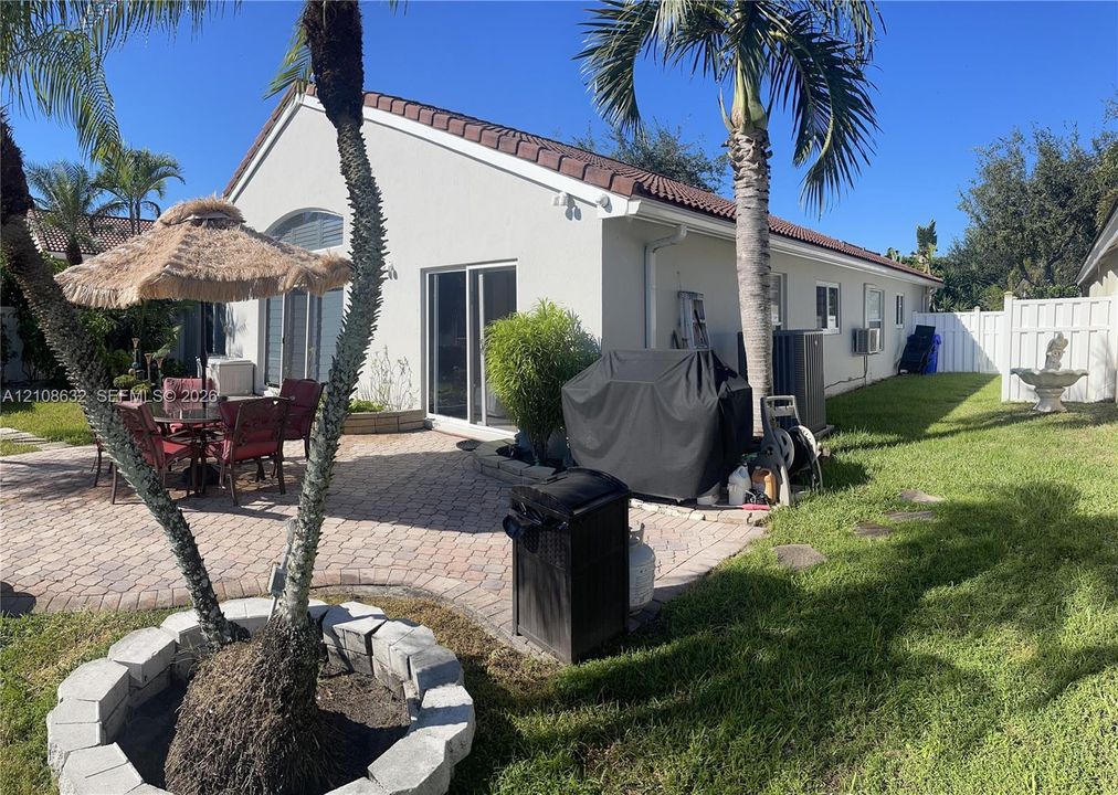 Rear yard featuring a paved patio, perimeter vinyl fencing, and a stone-encircled planter bed