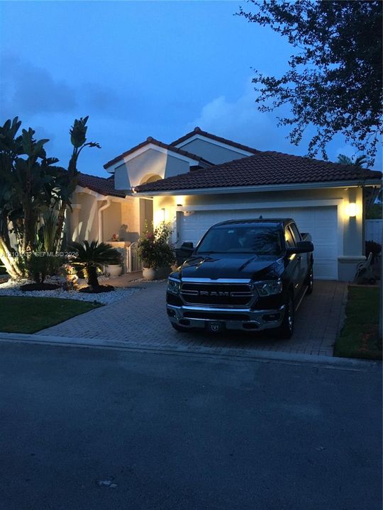 Single-story exterior featuring a clay tile roof, paved driveway, two-car garage, and established landscaping