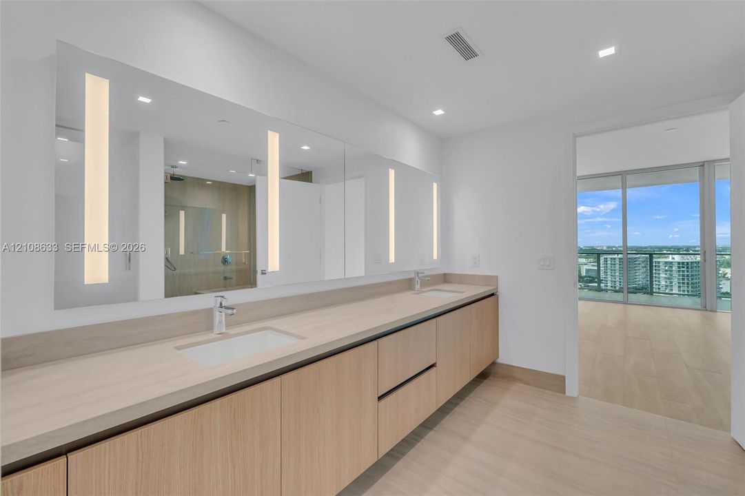 Floating vanity with integrated dual rectangular sinks, light wood-finish cabinetry, full-length illuminated wall mirror, and neutral-tone flooring