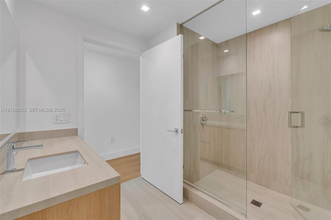 Modern bathroom featuring a wood-finish vanity with a solid-surface countertop, an integrated rectangular sink, a glass-enclosed walk-in shower with floor-to-ceiling tile, and recessed lighting