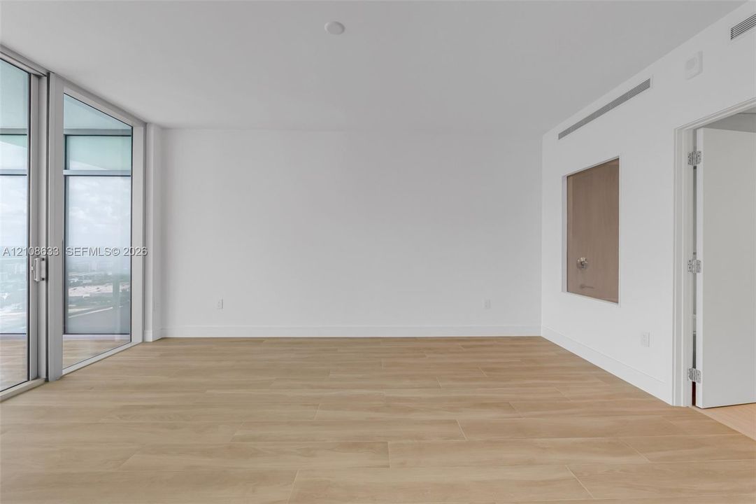 Interior space featuring floor-to-ceiling glass sliding doors, wood-finish tile flooring, recessed linear air conditioning vents, and a neutral color palette